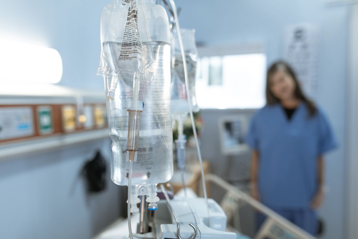 IV bags prepared for an infusion, with a nurse in the background